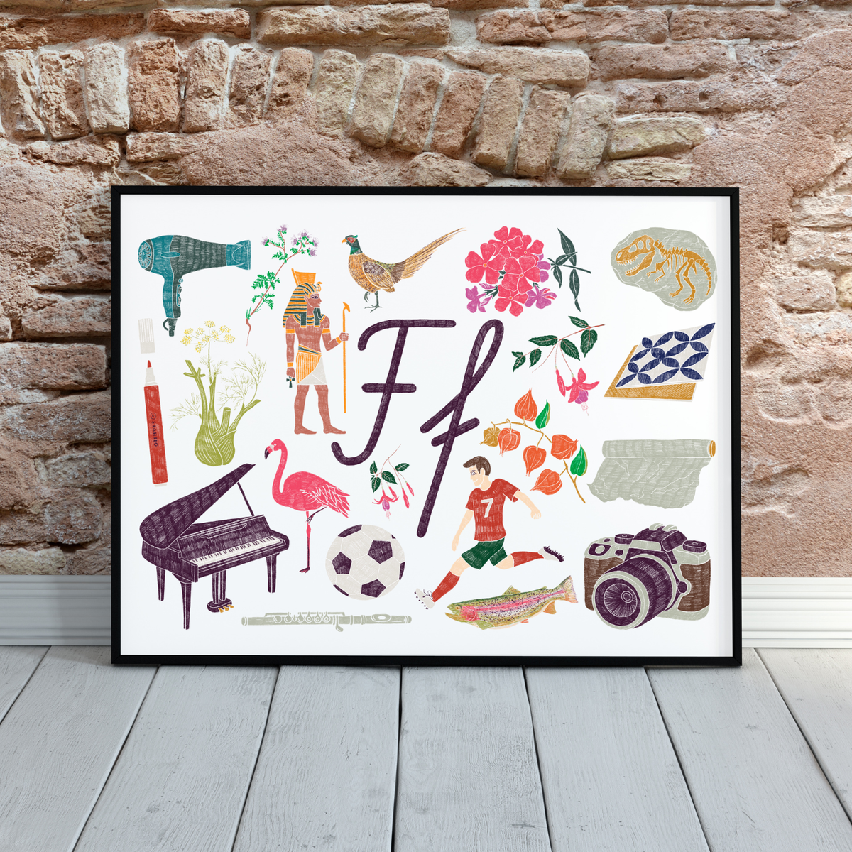 F burta plakāts melnā rāmī uz pelēkas dēļu grīdas, ķieģeļu siena.